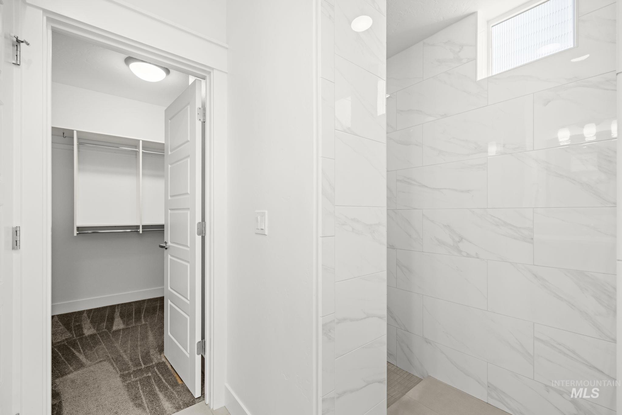 Bathroom with a marble-look tiled shower beside an open walk-in closet.