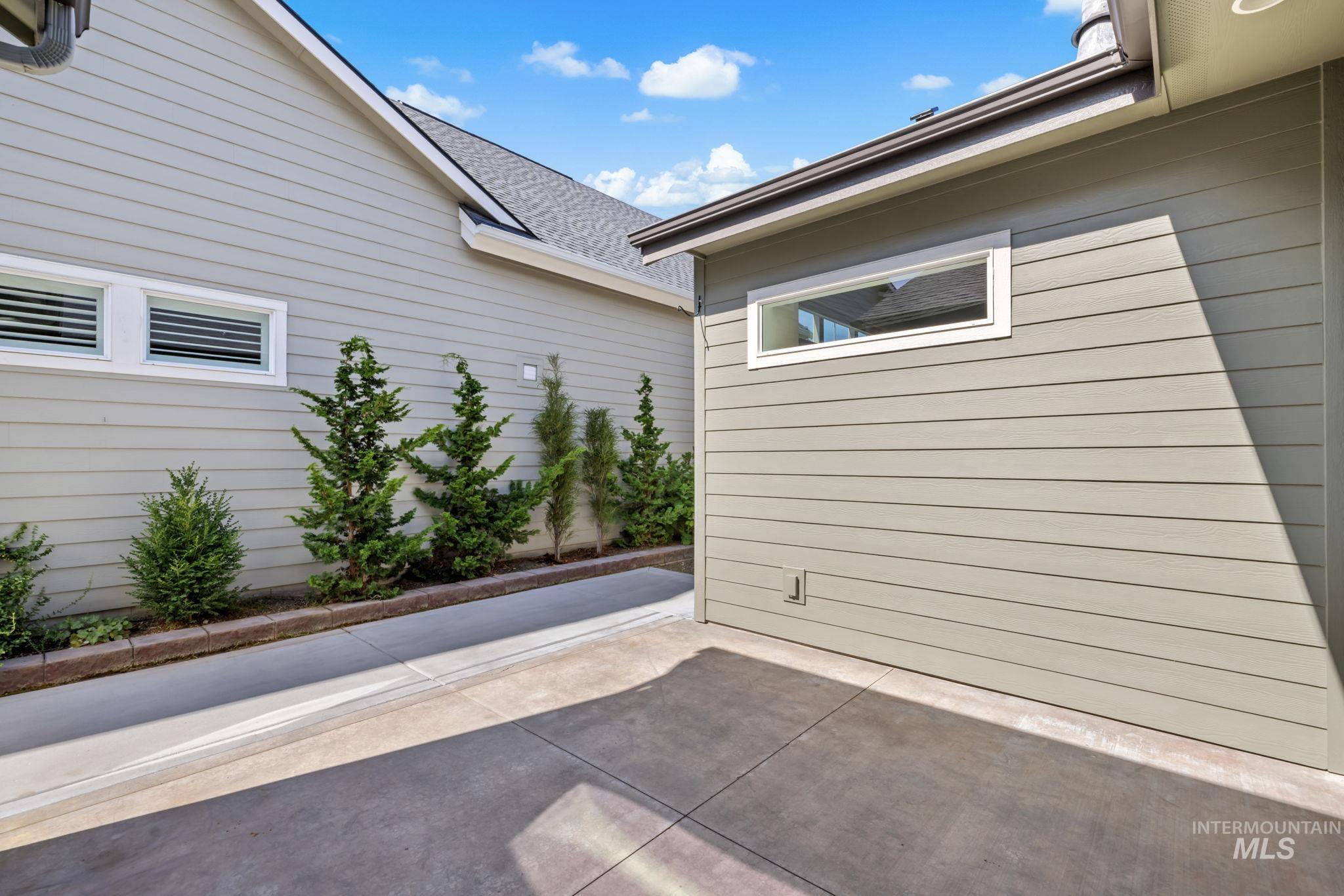 Paved courtyard between light-sided home walls, with narrow windows and landscaped shrubs.