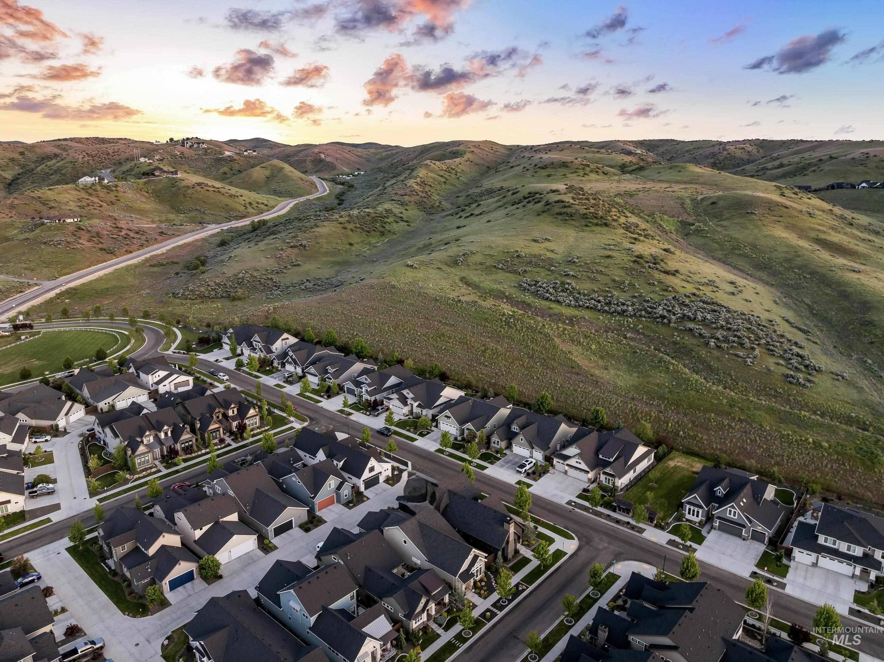 Aerial neighborhood beside rolling foothills, with a winding hillside road under a colorful dusk sky.