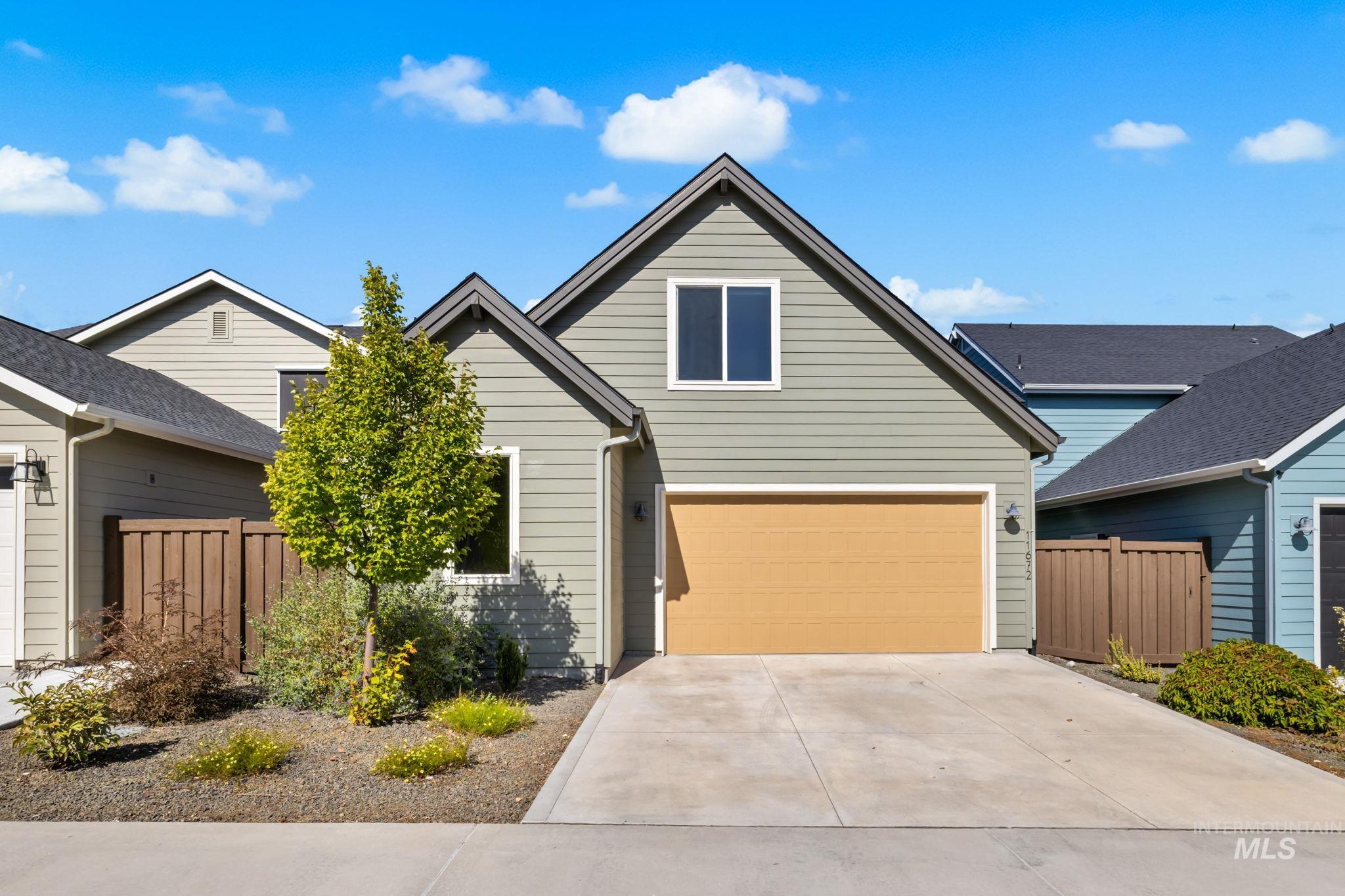 Gray gabled home with a tan double garage door, broad driveway, and landscaped front yard.