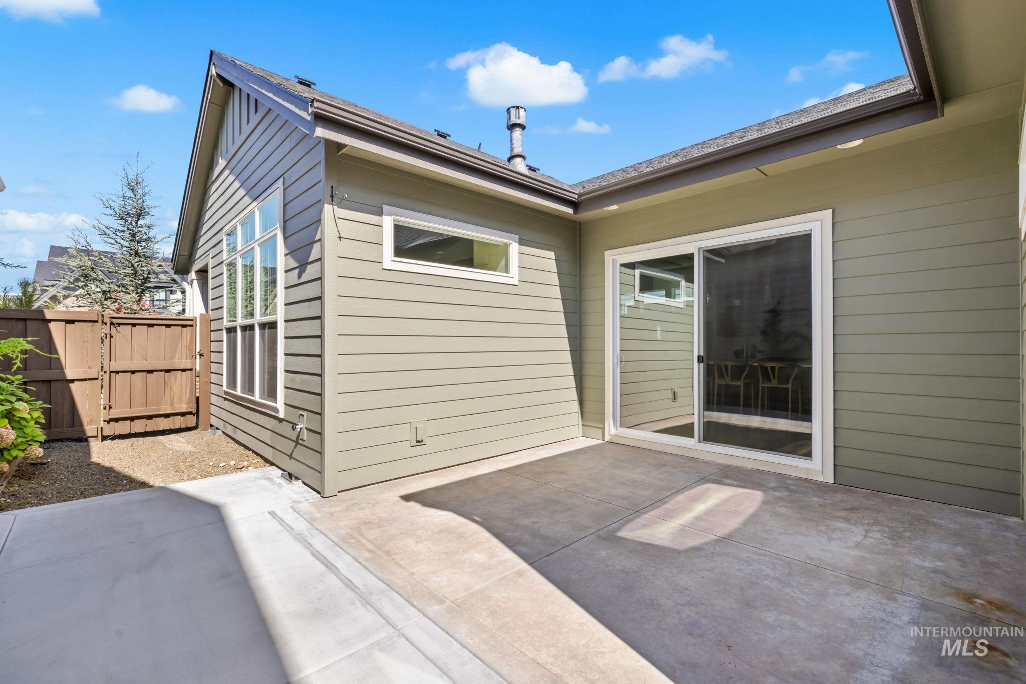 Home’s rear patio with sliding glass door, large windows, and wooden side gate.