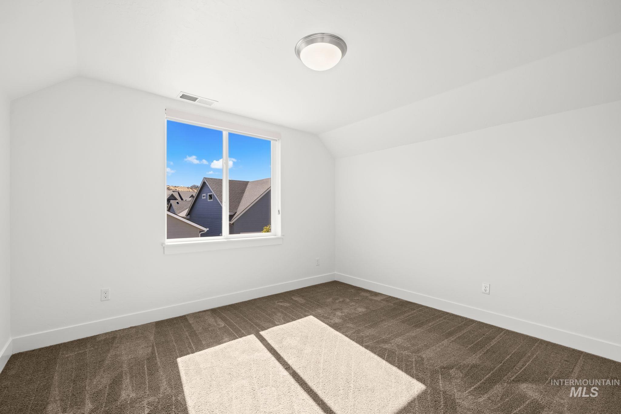 Empty bedroom with brown carpet and a sunny window overlooking neighboring homes.