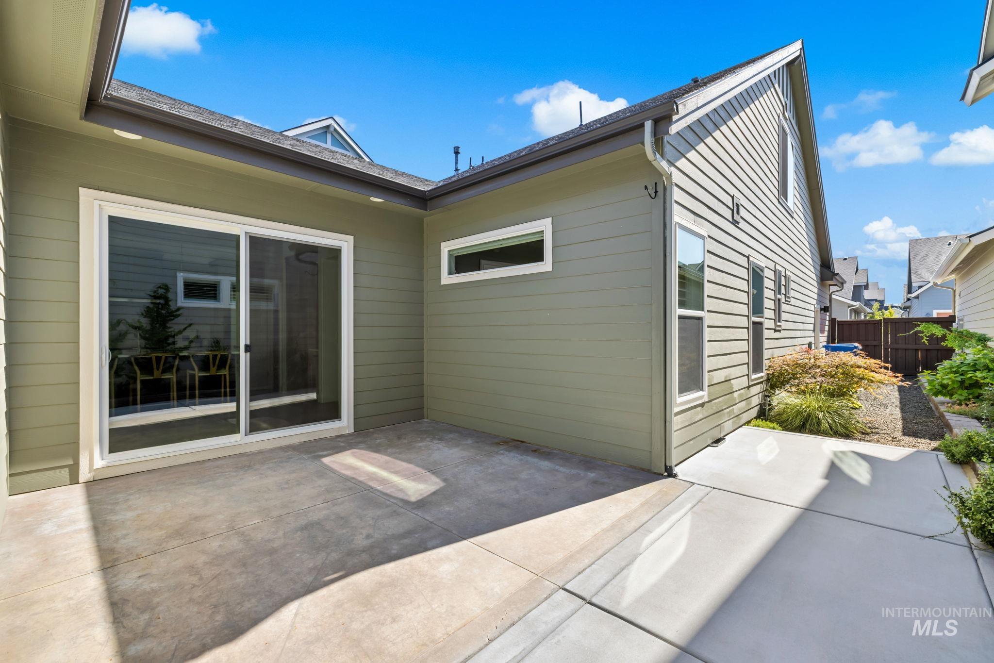 Concrete patio behind a two-story home, with a sliding glass door and landscaped side yard.