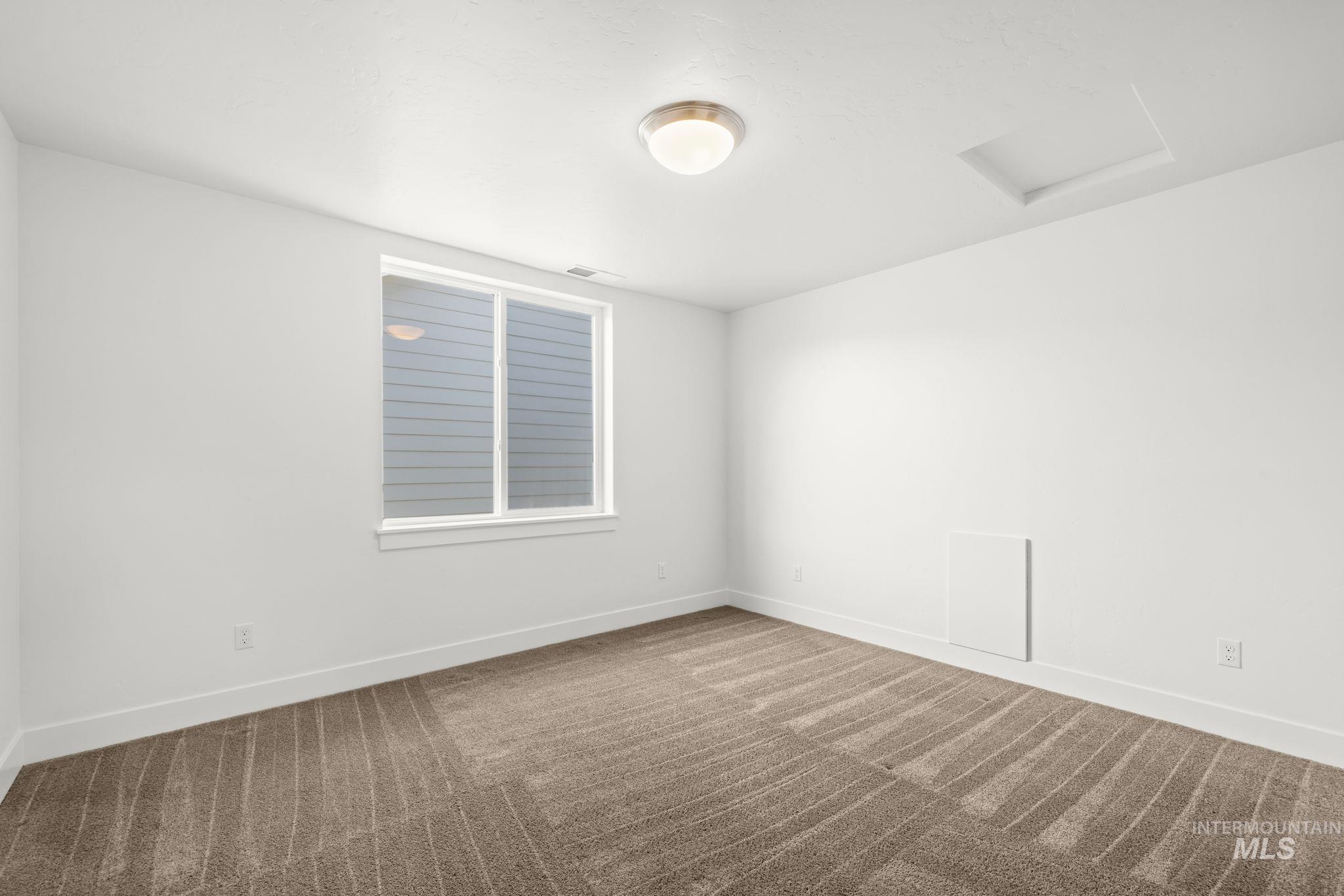 Empty bedroom with beige carpet, a window, and a ceiling access panel.