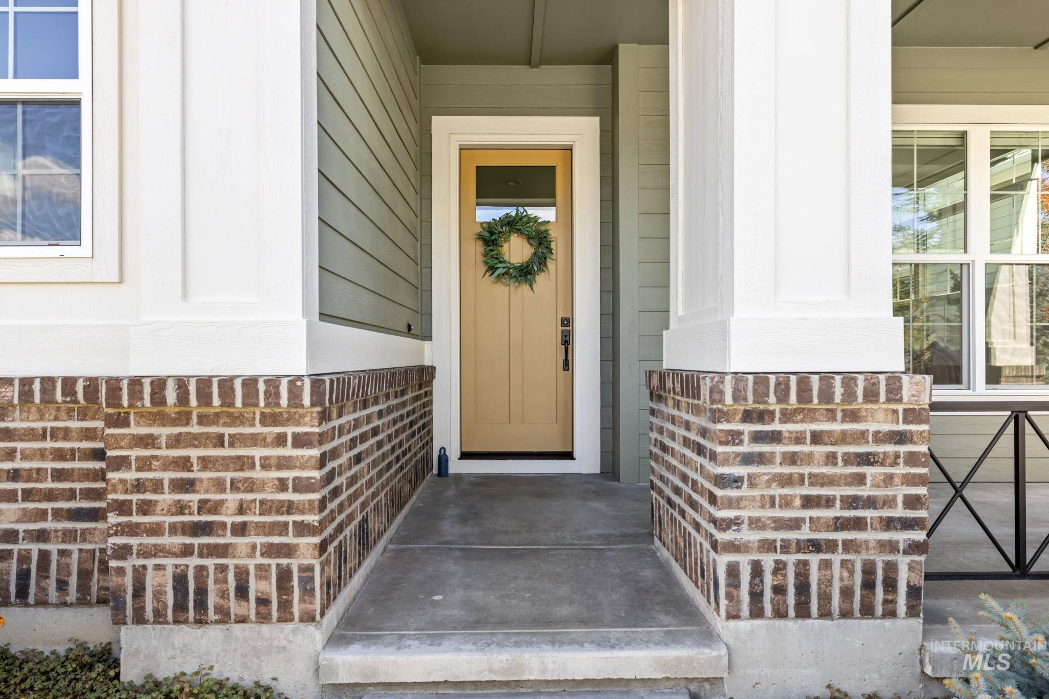 Home’s covered front porch with a wreath on the tan door and brick columns.