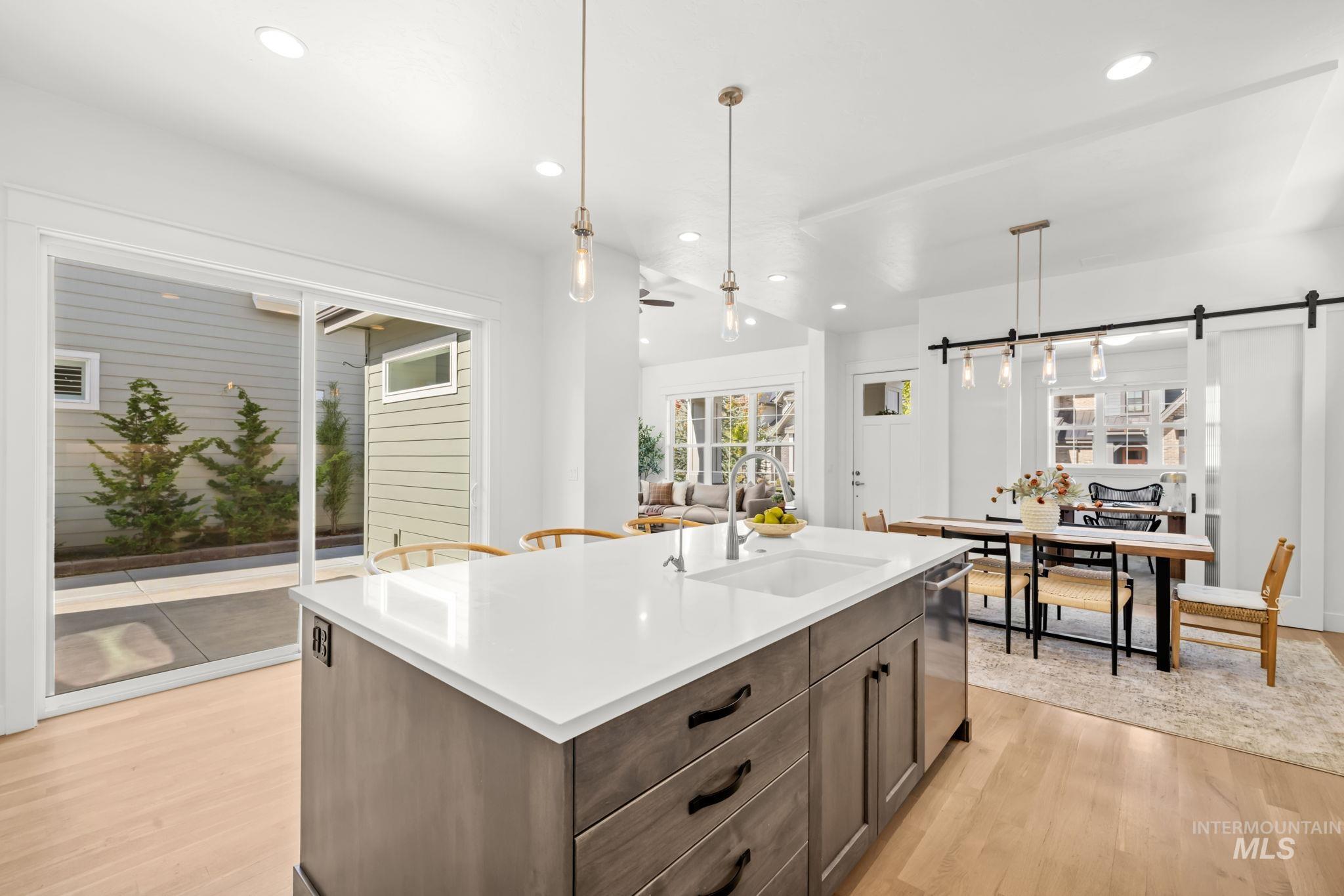 Open kitchen and dining area with a large white island, gray cabinetry, and sliding glass doors to a courtyard.