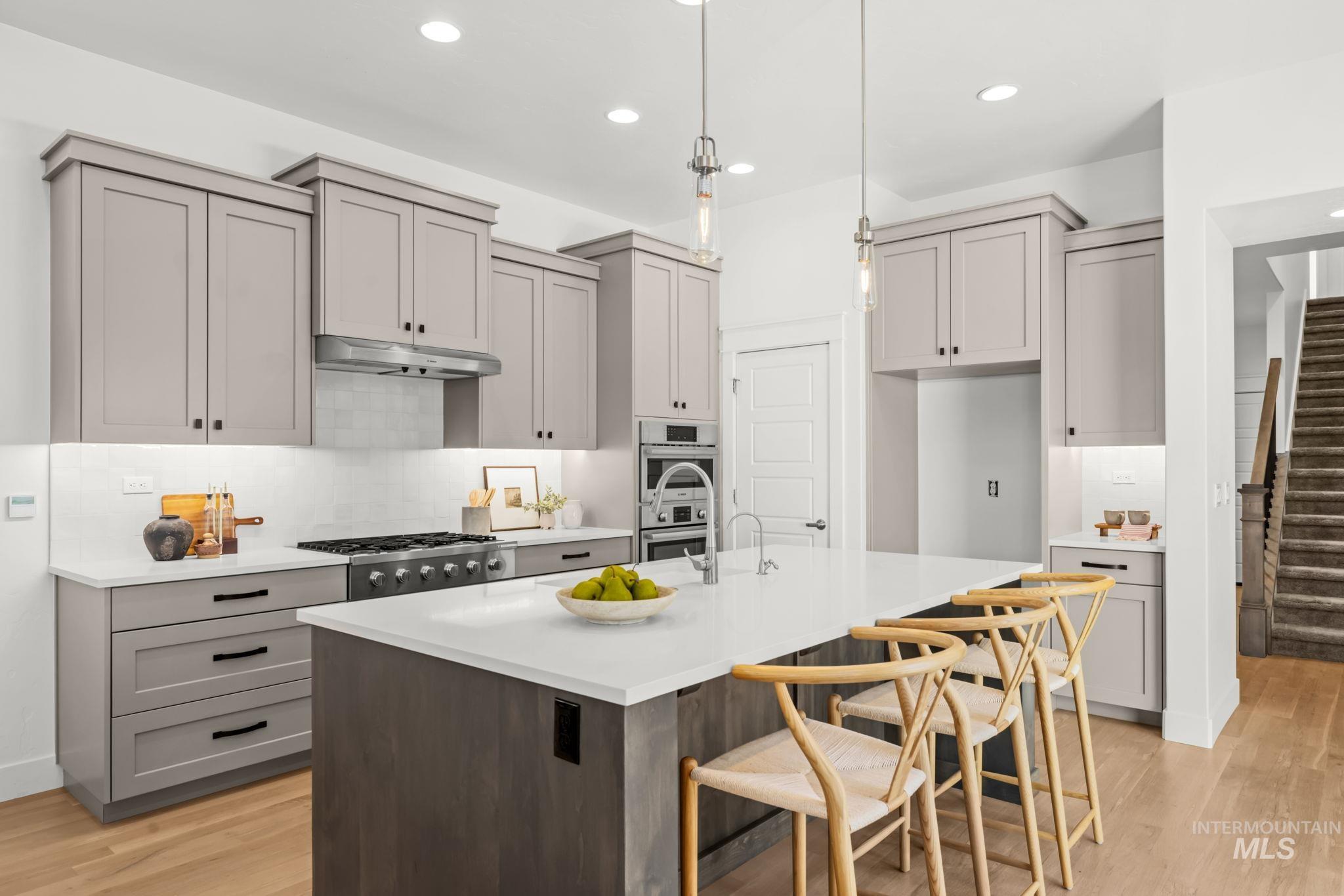 Kitchen with gray cabinets, stainless appliances, and a large island lined with wooden stools.