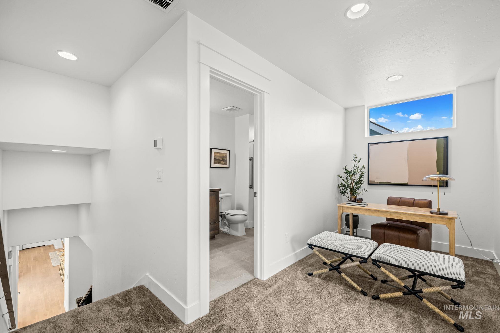 Furnished upstairs loft with a desk and striped benches beside an open bathroom doorway.