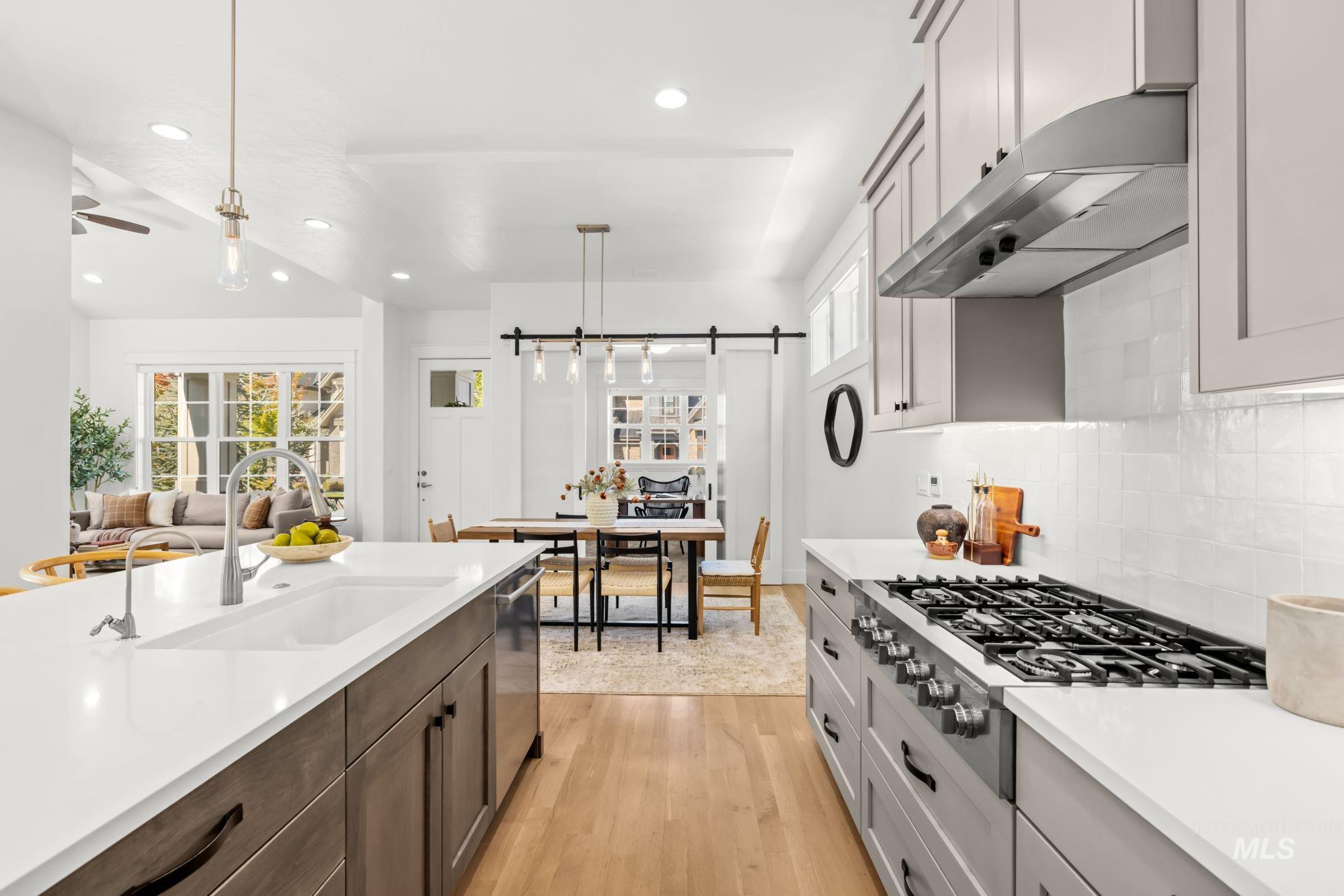 Bright kitchen with a large gas range and island, opening to a dining area and living room.