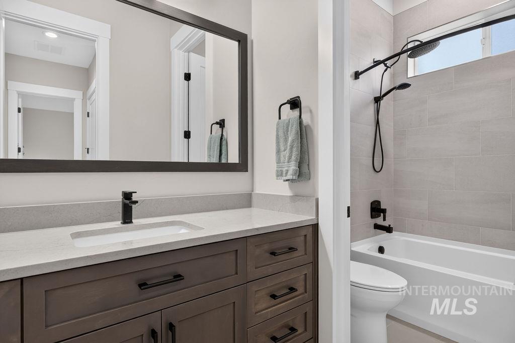 Bathroom with a gray wood vanity, large mirror, and white tub with tiled shower.