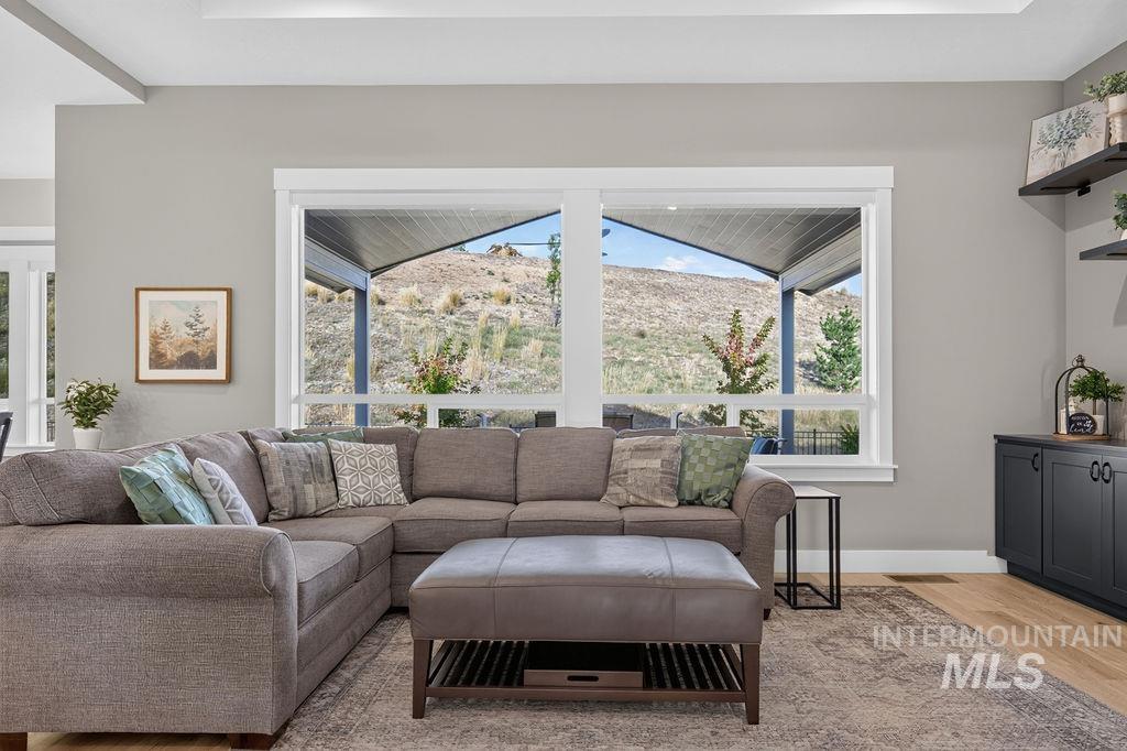 Living room with a gray sectional and ottoman facing wide windows overlooking a hillside.