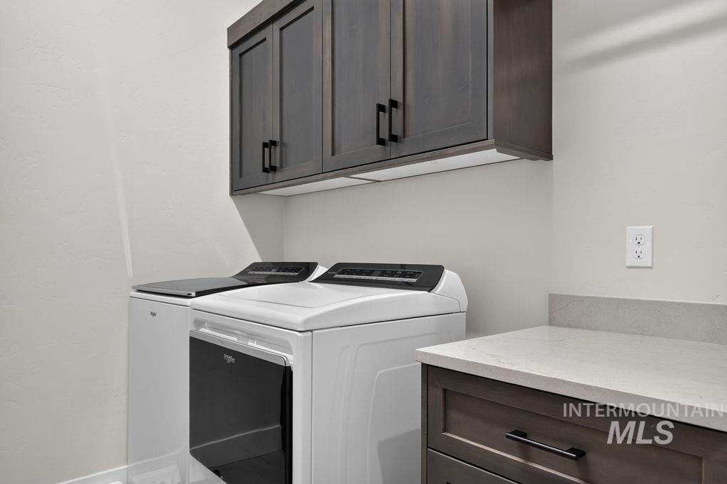 Laundry room with white washer and dryer, dark cabinets, and a stone countertop.