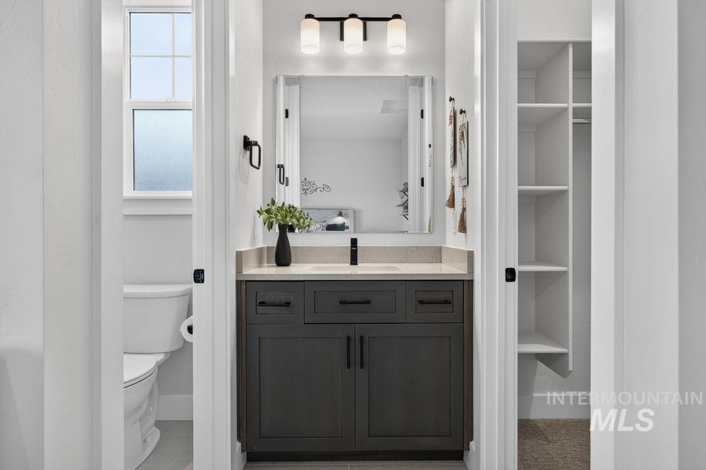 Bathroom vanity with dark cabinetry, a large mirror, and a three-light fixture; toilet and closet shelving flank it.
