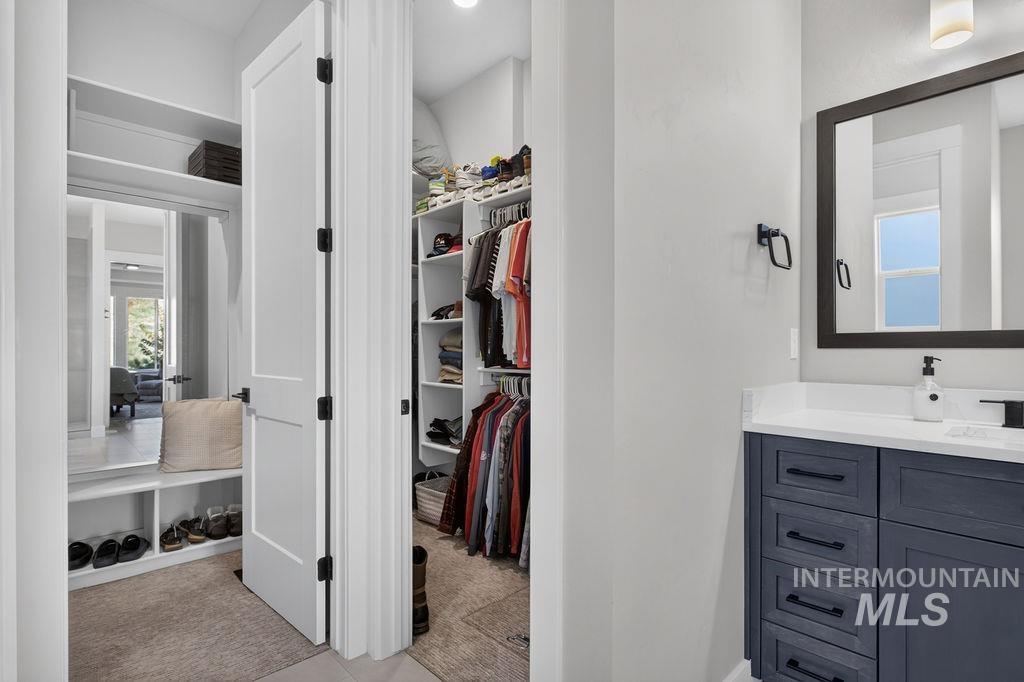 Walk-in closet with hanging clothes and shoe shelves beside a dark blue bathroom vanity.