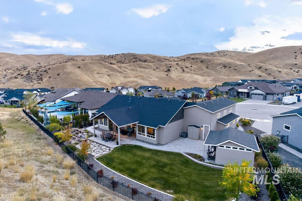 Aerial view of a home with a fenced lawn and patio, backed by open hills.