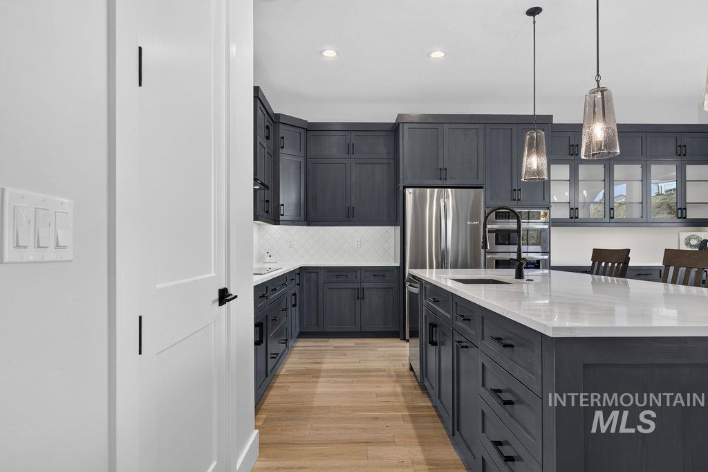 Modern kitchen with dark cabinetry, a white island, stainless steel appliances, and wood floors.