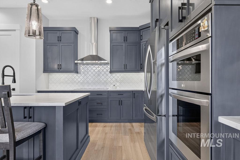 Modern kitchen with dark blue-gray cabinetry, a large island, patterned backsplash, and stainless steel appliances.