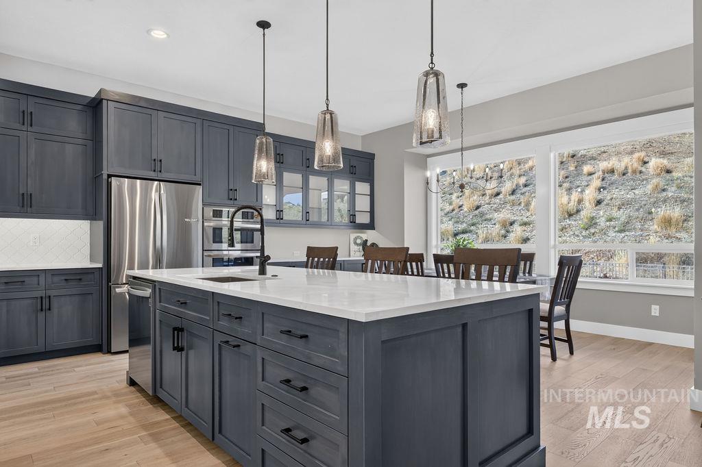 Modern kitchen with dark cabinets, a large white island, pendant lights, and windows overlooking a rocky hillside.