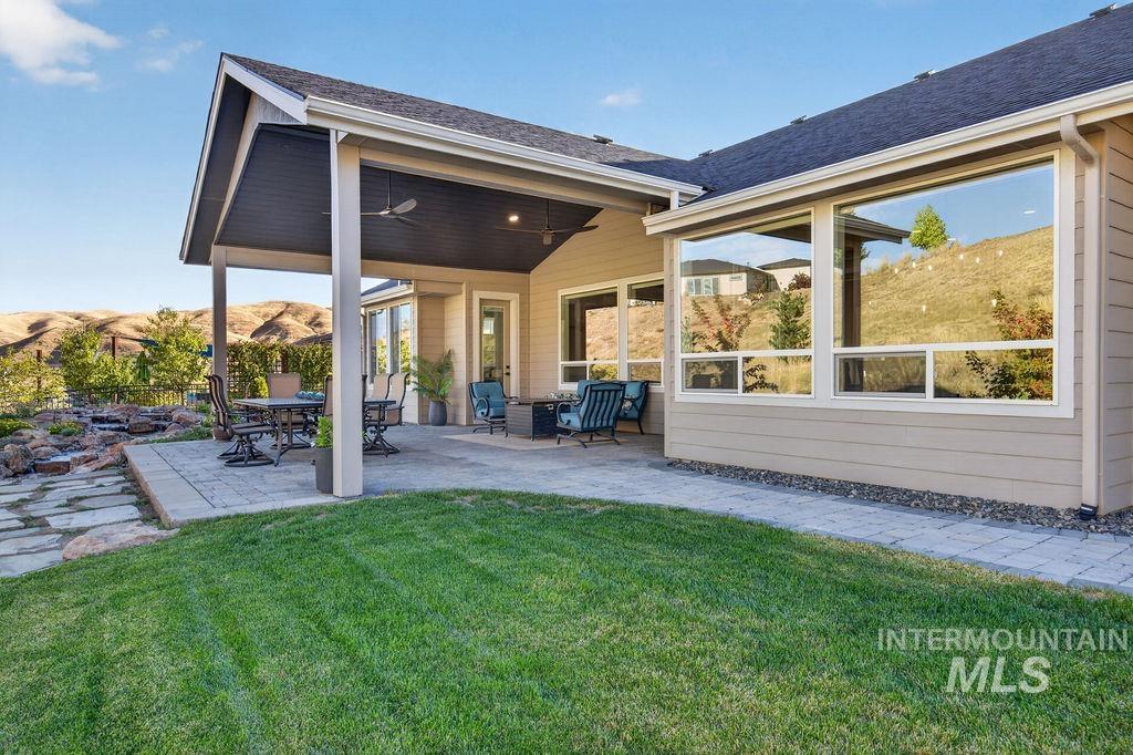 Covered backyard patio with outdoor seating beside a broad lawn and dry hills.