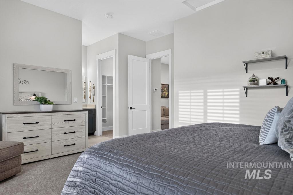 Bedroom with a gray quilted bed, light wood dresser, and sunlight filtered through blinds.