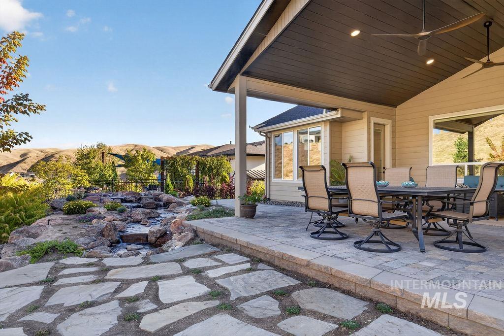 Covered patio with outdoor dining furniture, a stone path, and landscaped garden overlooking rolling hills.
