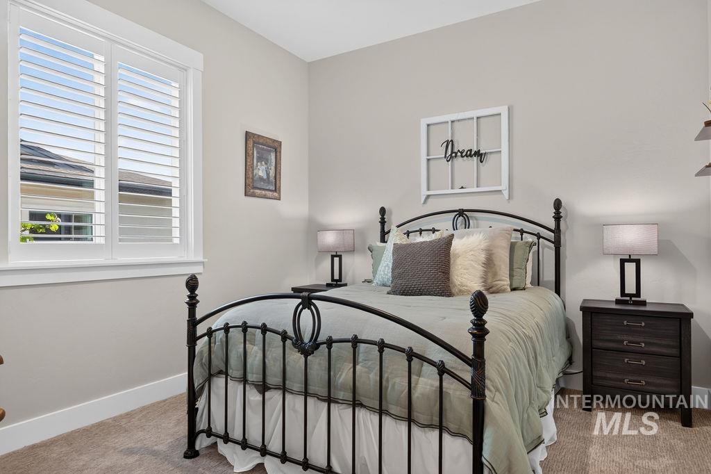 Bedroom with a black metal bed, pale green bedding, and white plantation shutters.