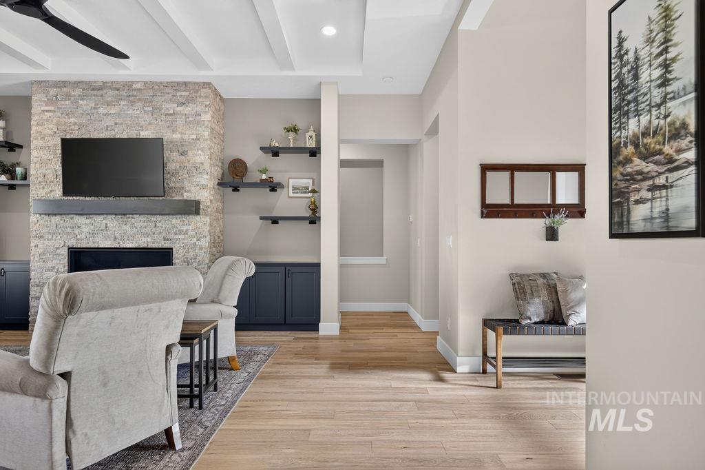Living room with a stone fireplace, mounted television, gray seating, and light wood floors.