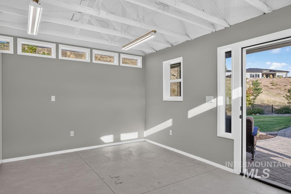 Vacant concrete-floor room with exposed white ceiling beams, high windows, and a glass door to the yard.