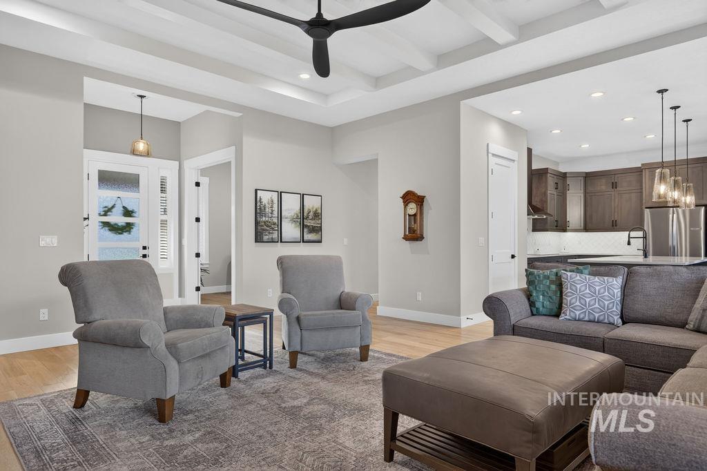 Furnished living room with gray seating, coffered ceiling, and an open kitchen.