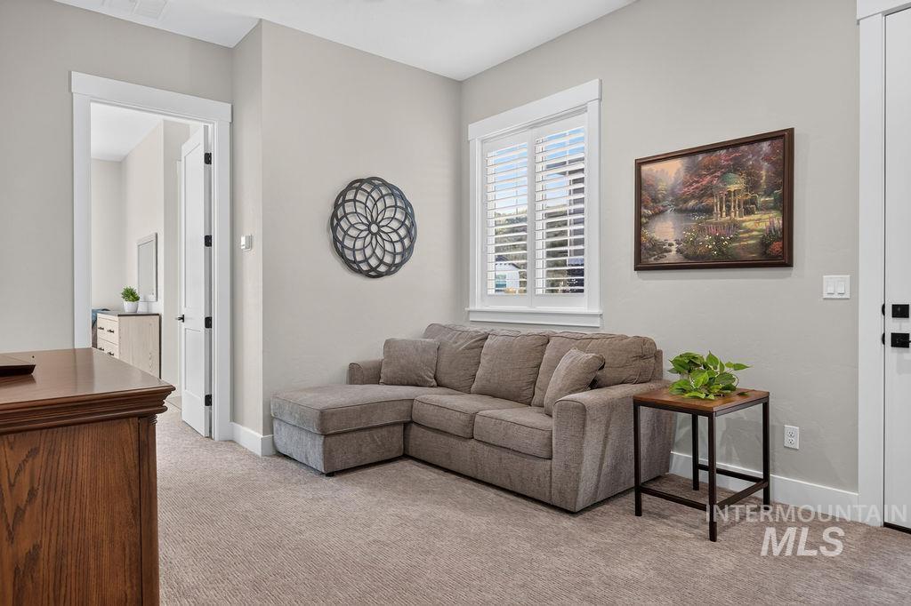 Sitting room with a gray sectional sofa, shuttered window, landscape painting, and small plant table.