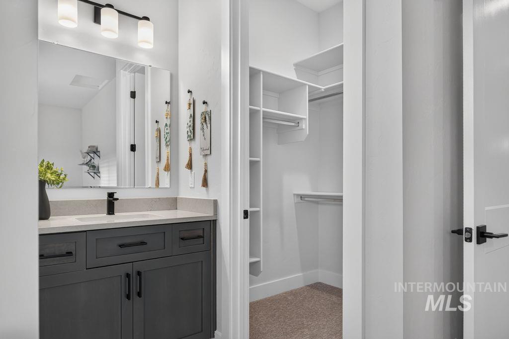 Bathroom vanity with dark cabinetry and black faucet beside an open walk-in closet.