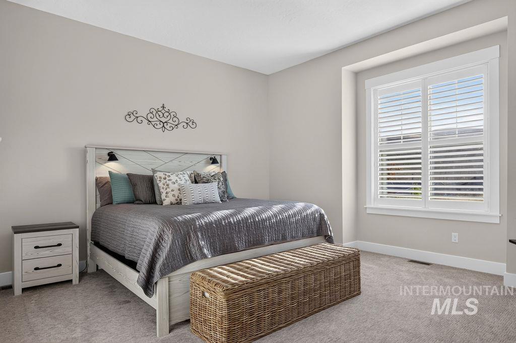 Furnished bedroom with a gray bed, woven storage bench, and large shuttered window.
