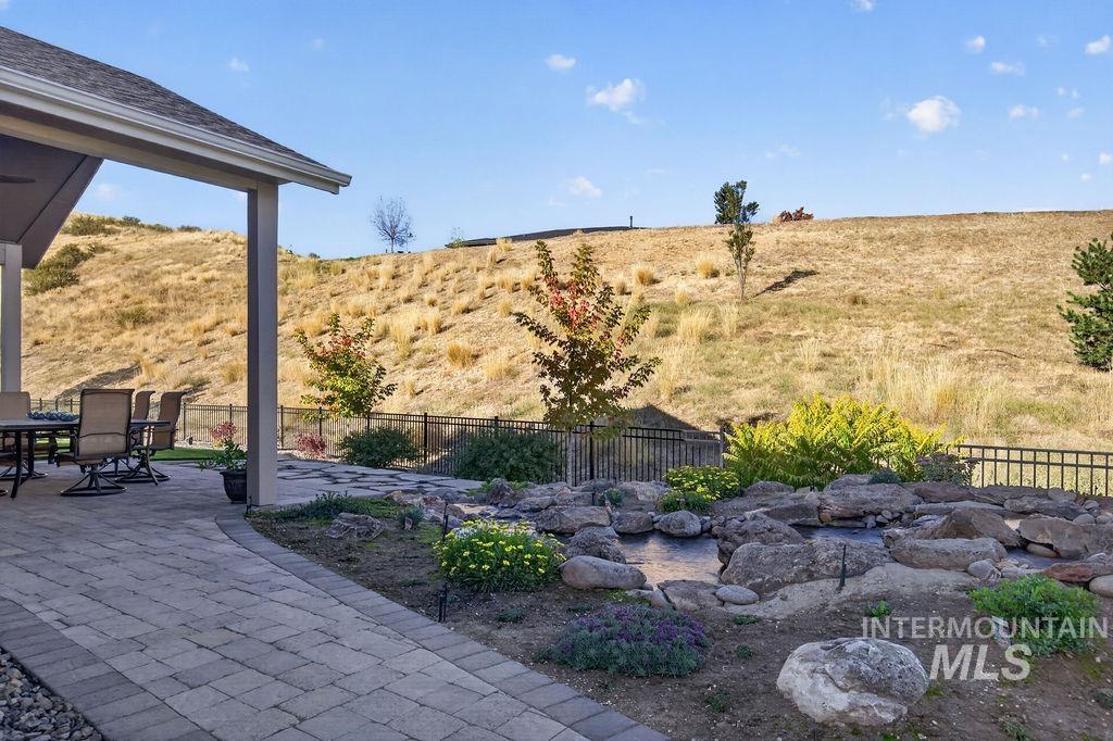 Backyard patio with outdoor seating, a rock water feature, and a dry grassy hillside beyond the fence.