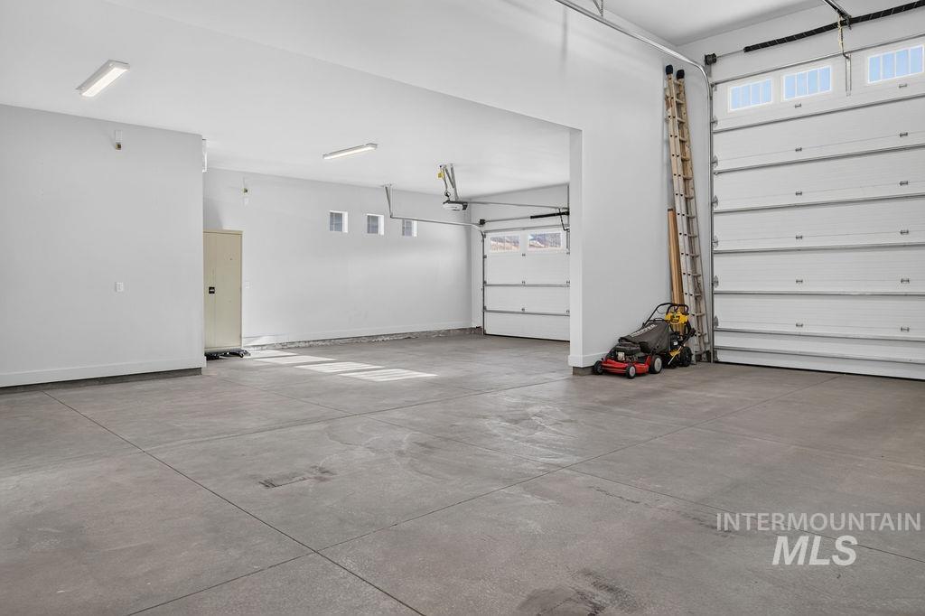 Spacious garage with a concrete floor, multiple overhead doors, and a ladder and mower.