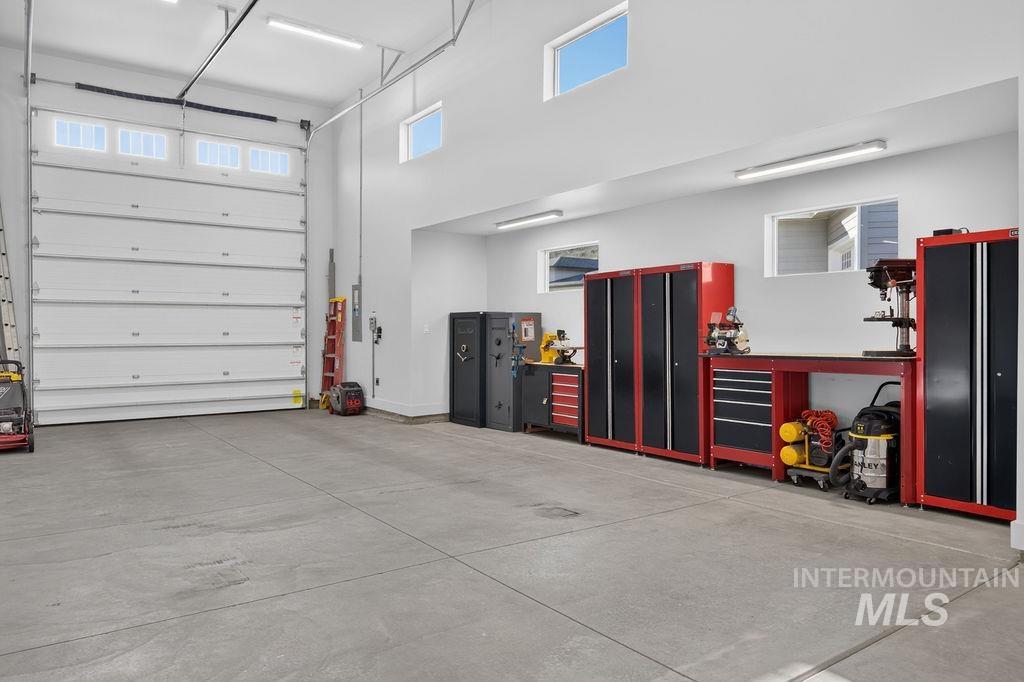 Spacious garage workshop with red-and-black tool cabinets, workbenches, and a large overhead door.