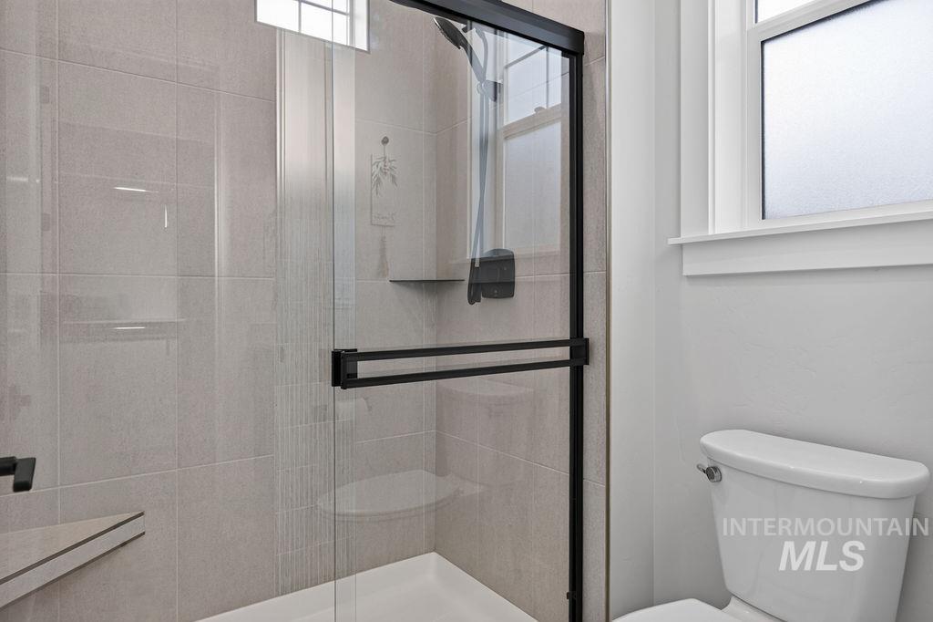 Bathroom with a black-framed glass shower, tiled walls, bathtub, and toilet beside a frosted window.