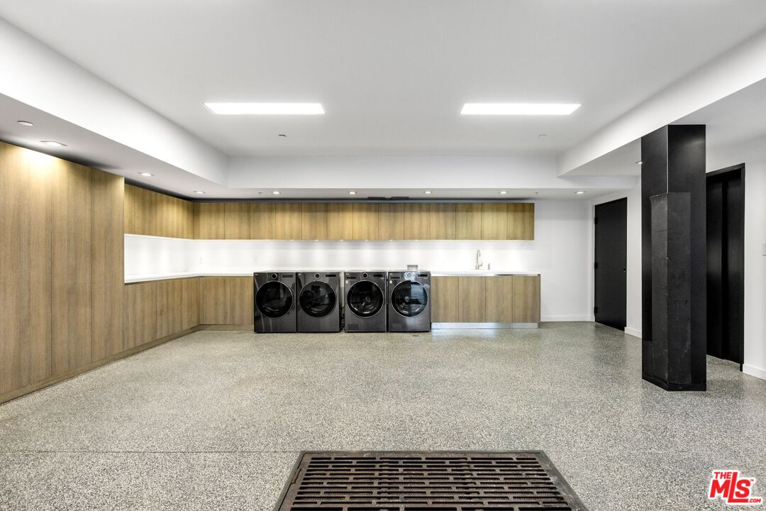 Laundry room with four front-loading machines, light wood cabinetry, and a long white counter.