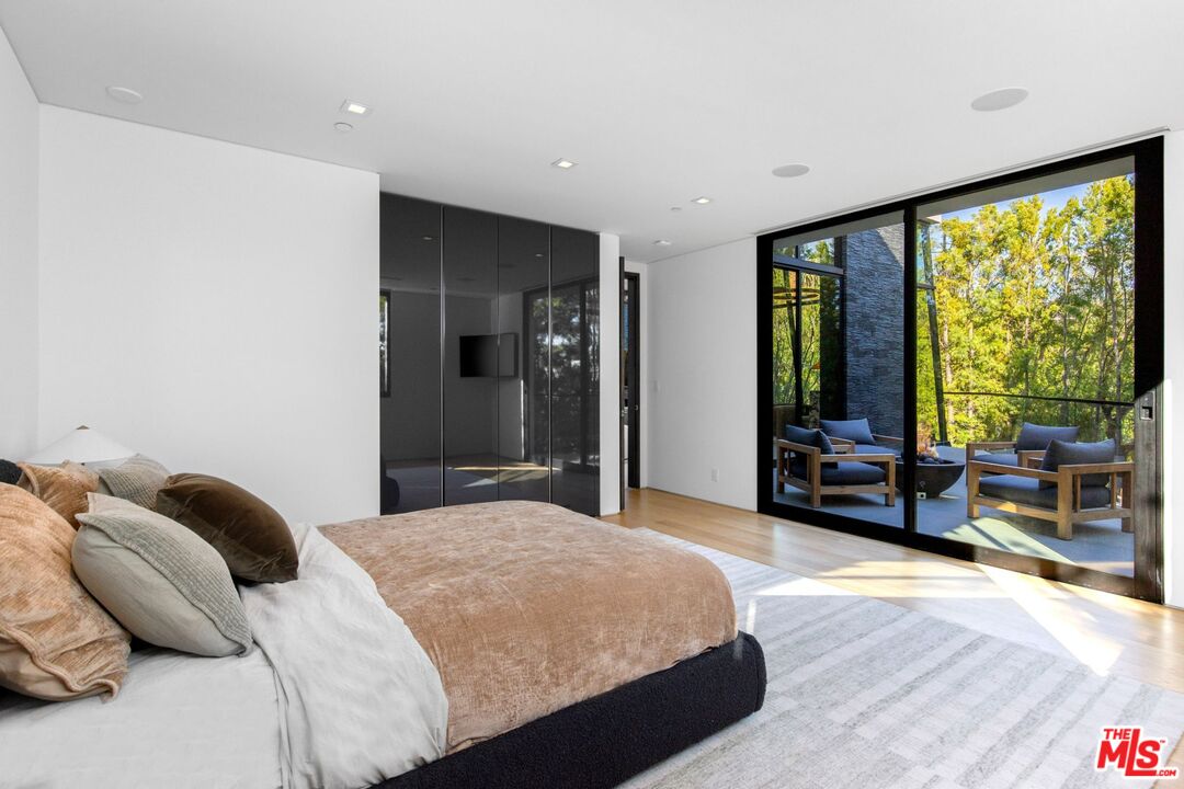 Modern bedroom with dark built-in wardrobes and sliding glass doors to a tree-lined patio.