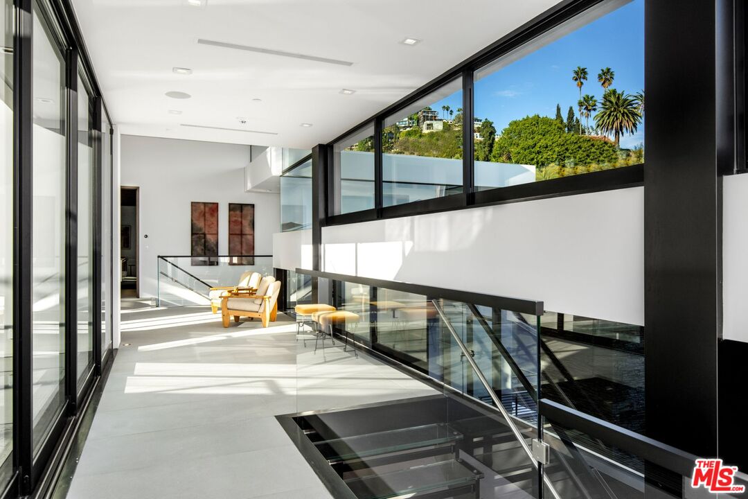 Modern upper-level landing with glass railings, black-framed windows, and hillside views.