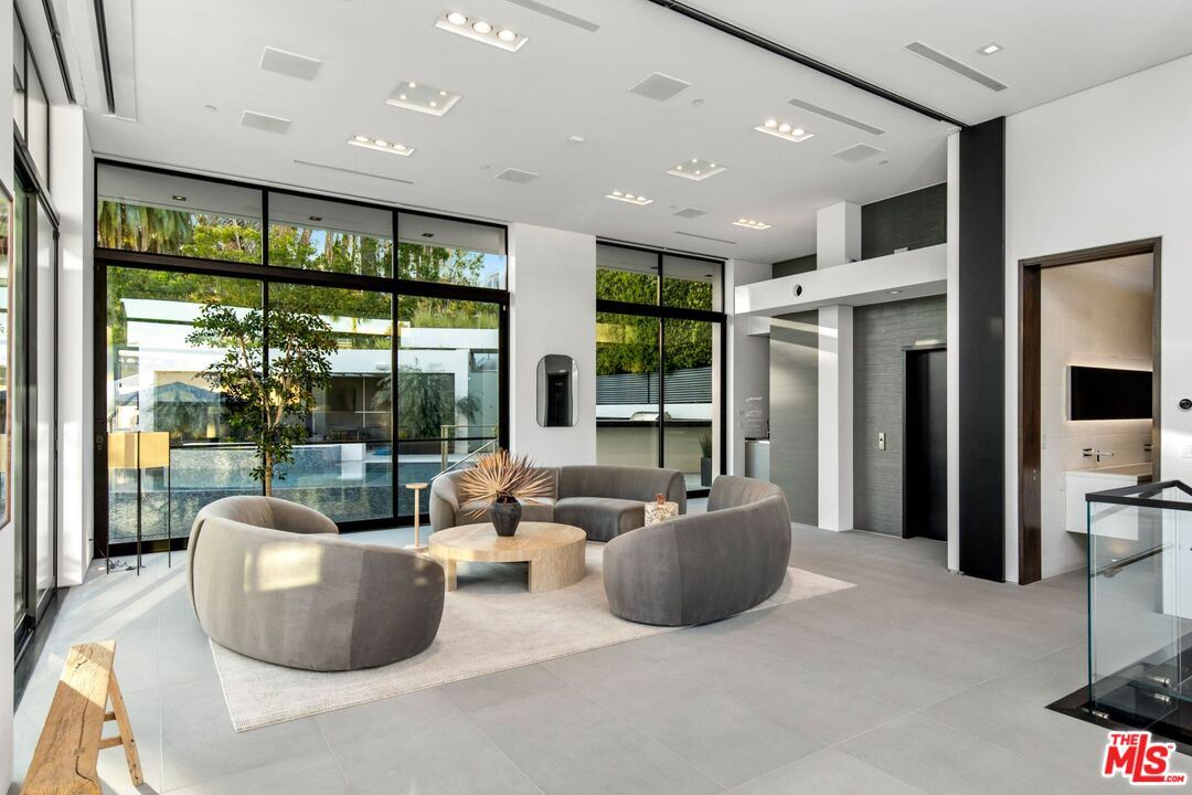 Modern living room with curved gray sofas and floor-to-ceiling windows overlooking a pool.
