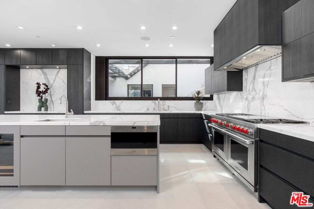 Modern kitchen with a marble island, dark cabinetry, and stainless-steel range with red knobs.