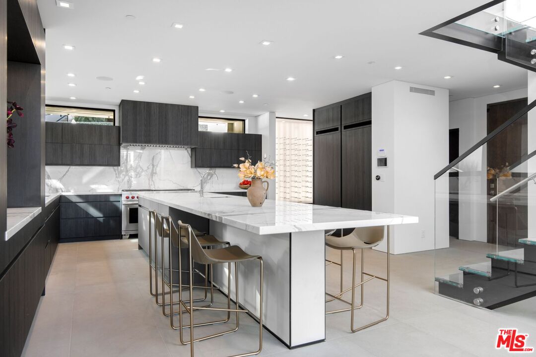 Modern kitchen with a white marble island, dark wood cabinetry, and a glass-railed staircase.