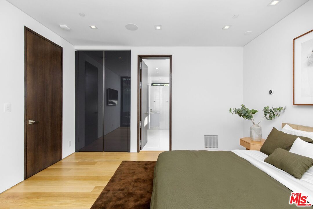 Modern bedroom with olive-green bedding, mirrored closet doors, and an open doorway to a white bathroom.