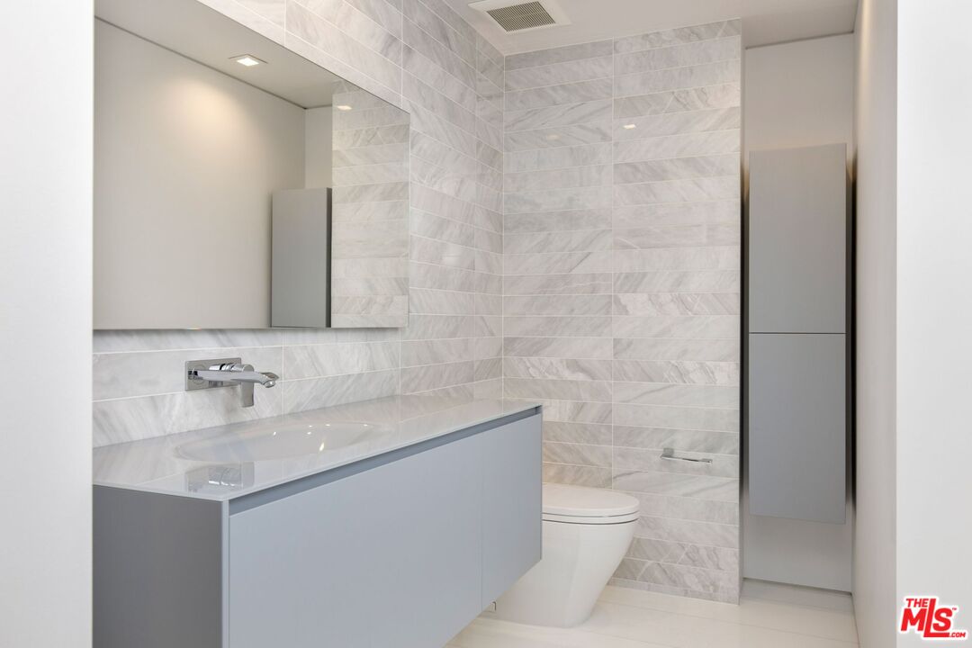 Modern bathroom with marble-look tile, a floating gray vanity, and a wall-mounted faucet.
