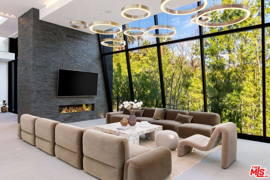 Modern living room with a stone fireplace, slanted glass walls, and neutral seating.