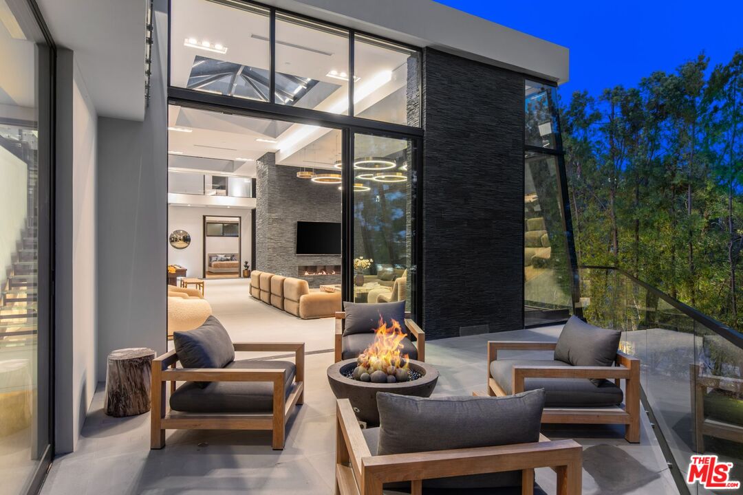 Modern patio with lounge chairs and a fire pit beside floor-to-ceiling glass walls.
