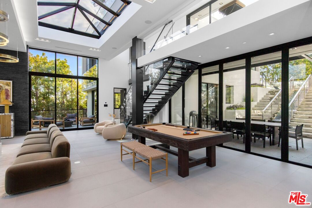 Double-height living room with a pool table, glass staircase, and floor-to-ceiling windows.