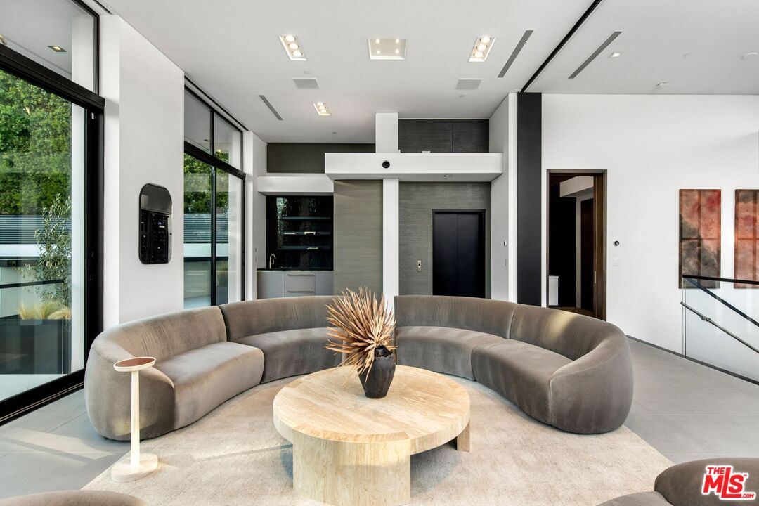 Modern living room with a curved gray sectional, round stone coffee table, and floor-to-ceiling windows.