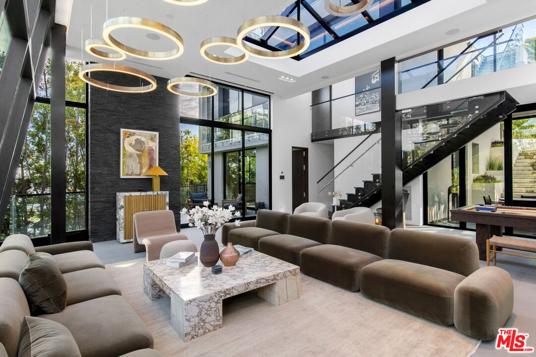 Double-height living room with floor-to-ceiling windows, ring pendant lights, and a black staircase.