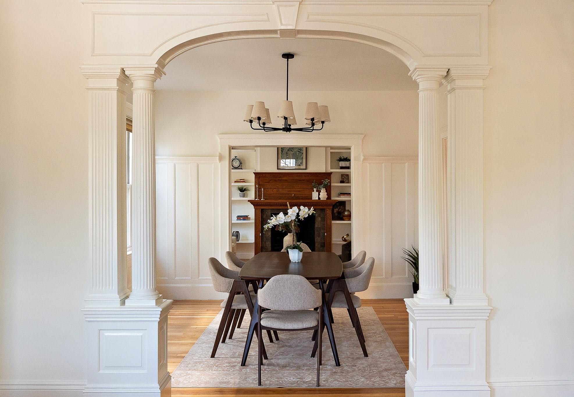Dining room with a grand columned arch, dark wood table, and fireplace with built-in shelves.